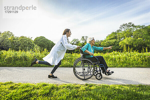 Sorglose Hausmeisterin vergnügt sich mit einer älteren Frau im Rollstuhl in einem öffentlichen Park
