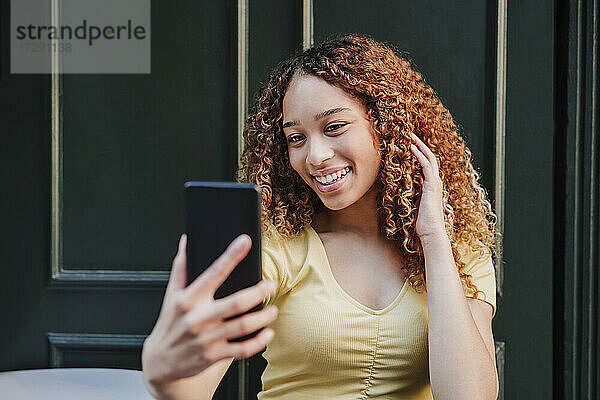 Schöne Frau mit Hand im Haar nimmt Selfie durch Handy