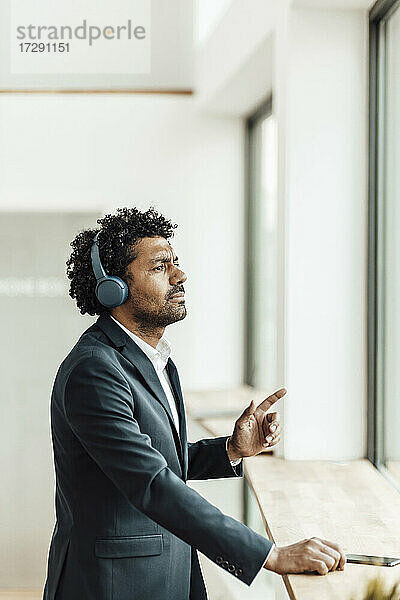 Männlicher Berufstätiger  der über drahtlose Kopfhörer im Büro Musik hört