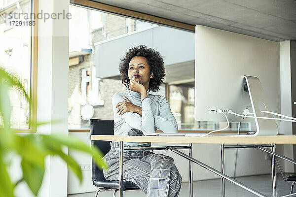 Unternehmerin mit Hand am Kinn  die am Schreibtisch im Büro sitzt und nachdenkt