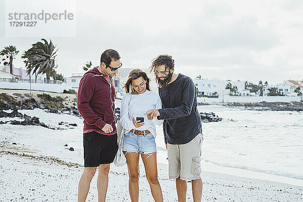 Freunde  die am Strand stehen und ein Mobiltelefon benutzen