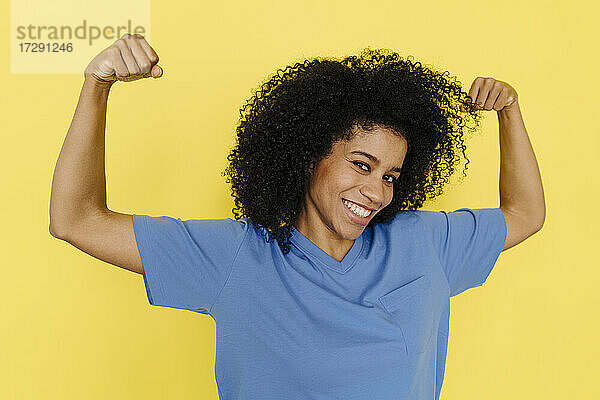 Lächelnde Frau  die Muskeln vor gelbem Hintergrund anspannt