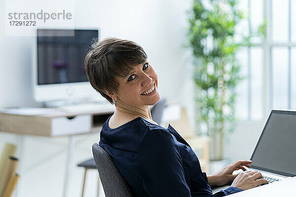 Lächelnde Geschäftsfrau sitzt mit Laptop im Büro