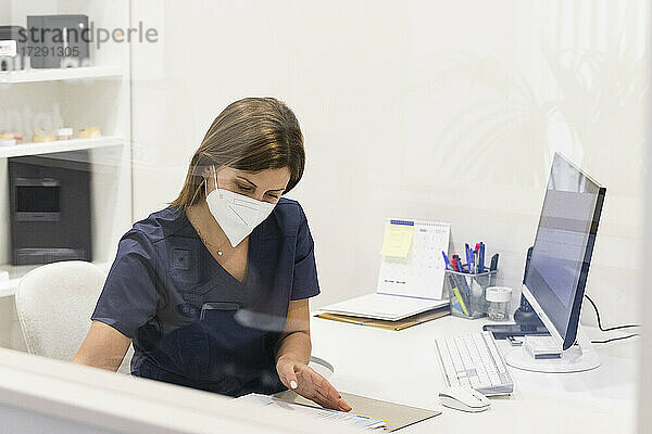 Zahnärztin mit Gesichtsschutzmaske bei der Arbeit am Schreibtisch in einer Klinik