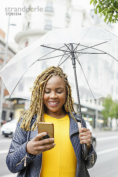 Lächelnde Frau  die ein Smartphone benutzt und einen Regenschirm hält