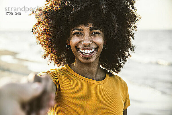 Afro-Frau lächelt  während sie die Hand ihres Freundes am Strand hält