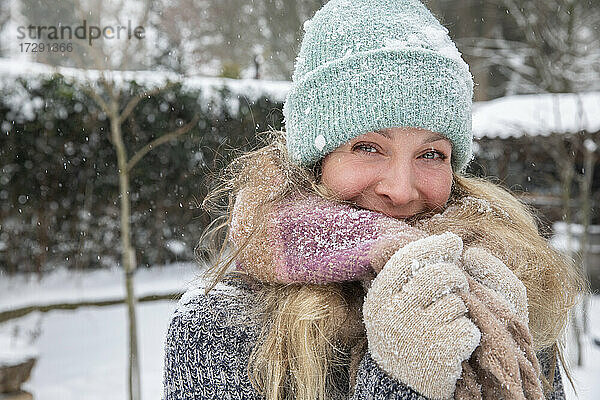 Blonde Frau bedeckt den Mund mit einem Schal  während sie bei Schnee im Hinterhof steht