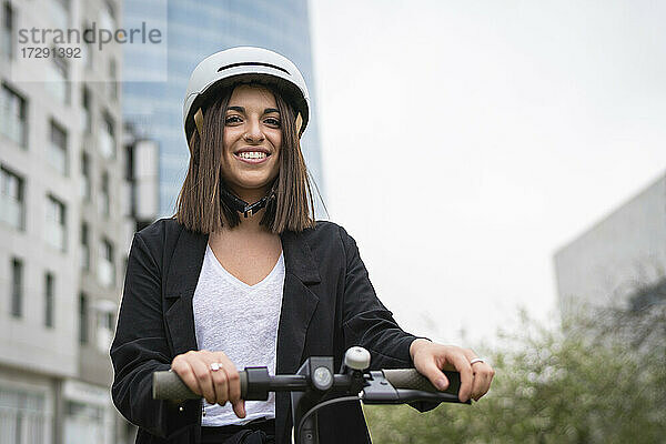 Geschäftsfrau mit Fahrradhelm  die lächelnd mit einem Elektroroller steht
