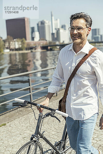 Lächelnder Geschäftsmann mit Fahrrad an einem sonnigen Tag