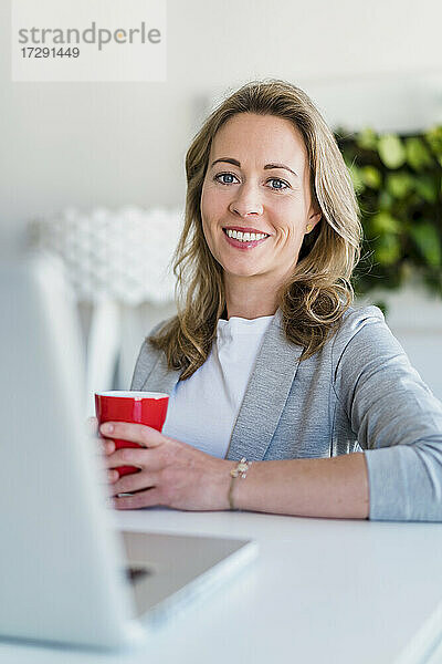 Lächelnde Unternehmerin beim Kaffee am Schreibtisch