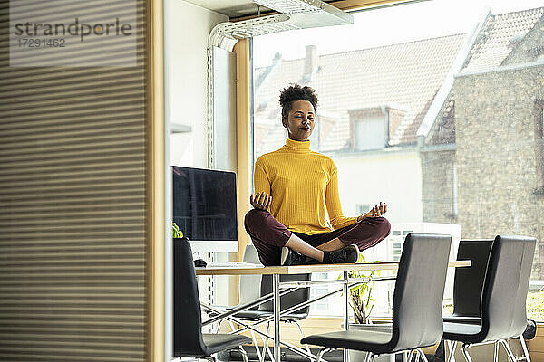 Geschäftsfrau beim Meditieren auf dem Schreibtisch im Büro sitzend