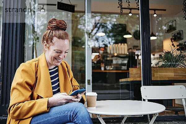 Lächelnde Frau  die ein Smartphone benutzt  während sie in einem Café sitzt