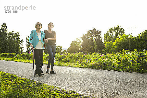 Mittlere erwachsene Frau  die eine ältere Frau beim Spazierengehen im Park stützt