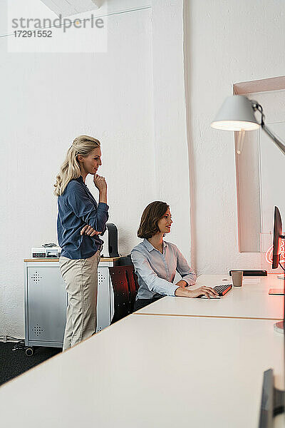 Junge Unternehmerin  die einen Computer benutzt  während ein Kollege im Büro sitzt und diskutiert