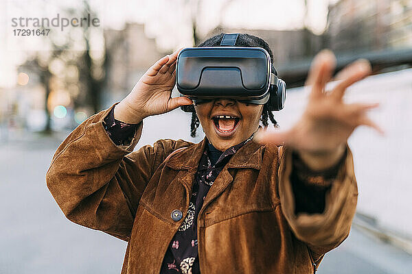 Fröhliche Frau  die ihre Hand ausstreckt  während sie einen Virtual-Reality-Simulator benutzt