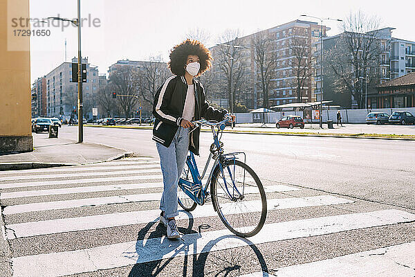 Frau mit Gesichtsschutz  die mit dem Fahrrad auf einer Straße in der Stadt unterwegs ist