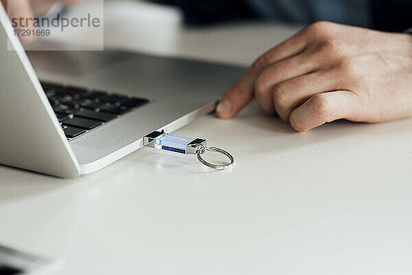 Geschäftsmann mit Laptop und eingestecktem USB-Stick auf dem Schreibtisch