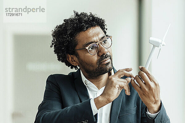 Männlicher Unternehmer mit lockigem Haar  der ein Windradmodell im Büro untersucht