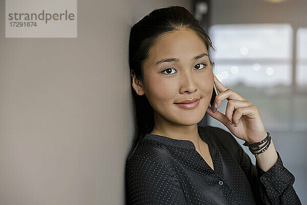 Lächelnde junge Frau  die im Büro mit einem Smartphone spricht