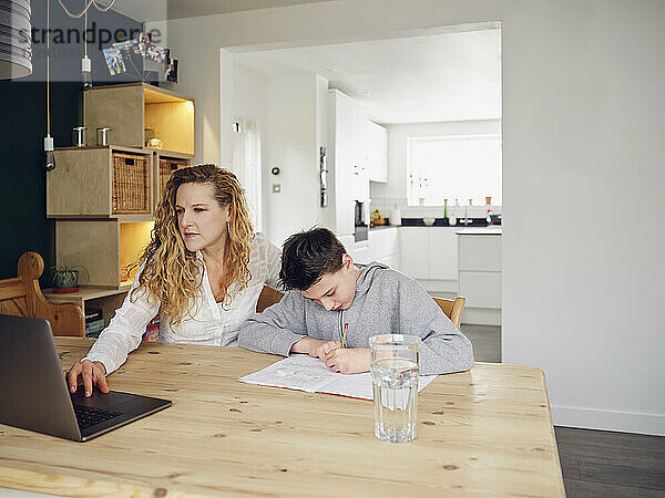 Blonde Frau benutzt Laptop bei ihrem Sohn  der zu Hause lernt