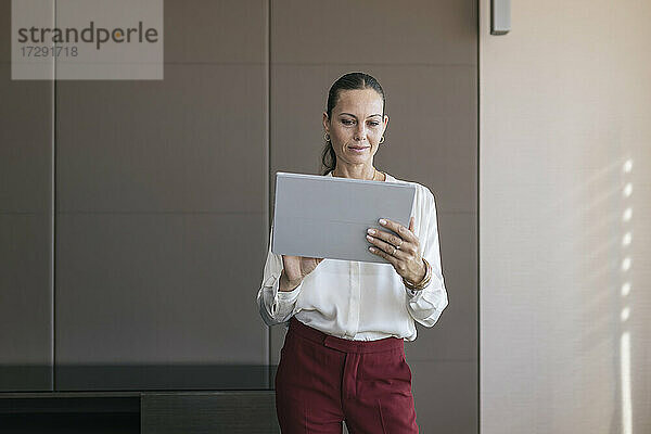Reife Geschäftsfrau  die im Stehen im Büro ein digitales Tablet benutzt