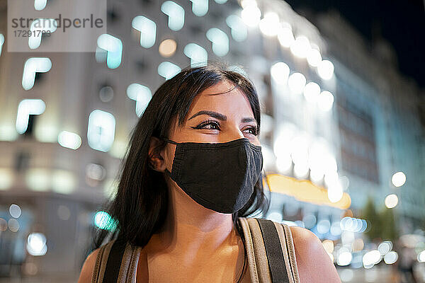 Junge Frau mit Gesichtsschutzmaske  die in der Dämmerung wegschaut