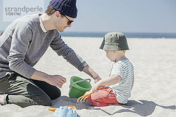 Vater und Sohn spielen zusammen mit Sandspielzeug am Strand