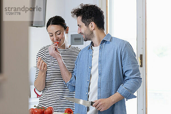 Lächelnder Freund füttert seine Freundin in der Küche zu Hause mit Tomaten