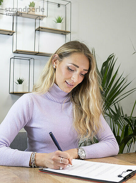 Weibliche Fachkraft mit blondem Haar beim Unterzeichnen von Dokumenten im Büro