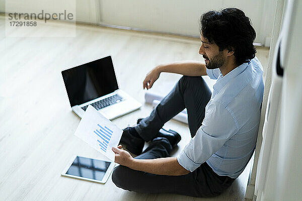 Geschäftsmann mit digitalem Tablet und Laptop  der ein grafisches Dokument im Büro analysiert