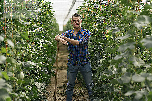 Lächelnder Landwirt mit landwirtschaftlichen Geräten auf einem Biohof