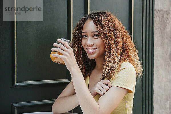 Junge Frau hält Orangensaftglas im Freien