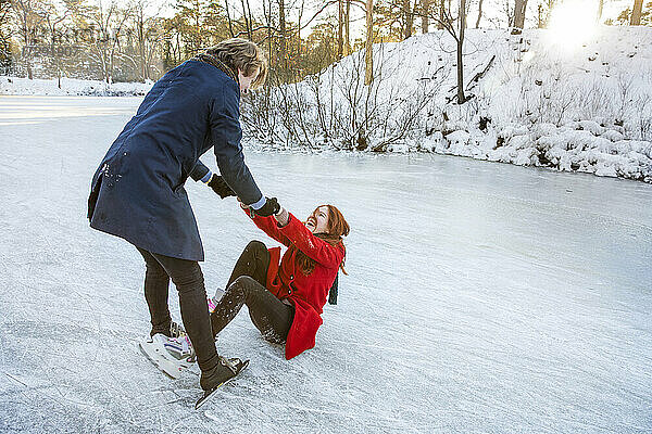Freund hält die Hände seiner Freundin  während er auf einem zugefrorenen See aufsteht