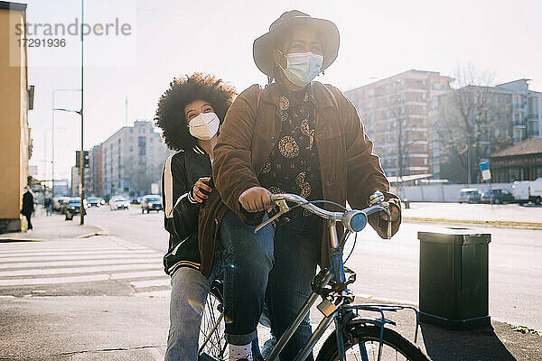 Frau mit Gesichtsmaske auf dem Fahrrad mit einem Freund auf dem Rücken in der Stadt