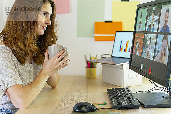 Freiberuflerin hält Tasse während eines Videogesprächs am Computer im Home Office