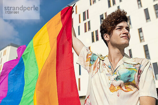 Junger Mann schaut weg  während er die Regenbogenflagge weht