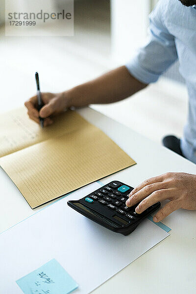Geschäftsmann schreibt in ein Buch und benutzt einen Taschenrechner im Büro