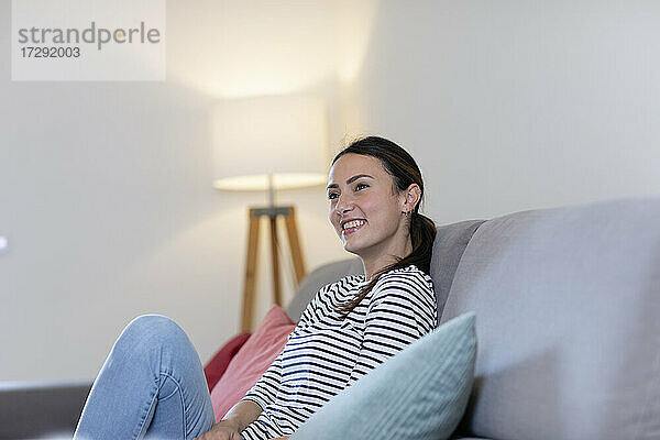 Lächelnde junge Frau  die zu Hause auf dem Sofa sitzt und träumt