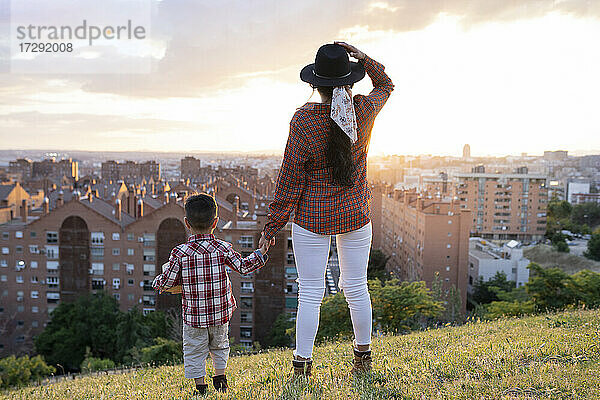 Mutter hält die Hand ihres Sohnes und blickt auf eine Stadtlandschaft auf einem Hügel