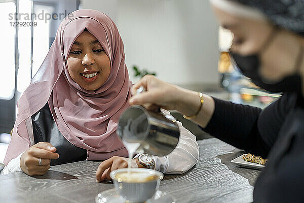 Lächelnde Frau wartet  während die Kellnerin in einem Café Milch in eine Tasse gießt