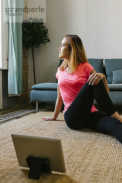 Rothaarige Frau  die ein digitales Tablet benutzt  während sie zu Hause Übungen macht