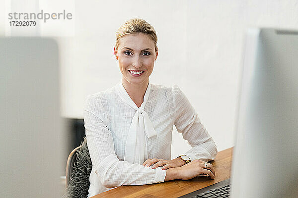 Schöne lächelnde blonde Geschäftsfrau sitzt am Schreibtisch im Büro