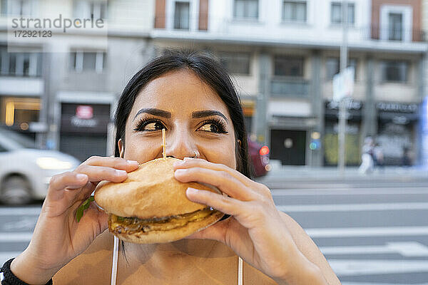 Junge Frau isst einen Hamburger in einem Straßencafé in der Abenddämmerung