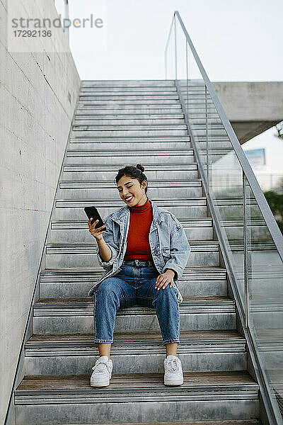 Junge Frau benutzt ein Mobiltelefon  während sie auf einer Treppe sitzt