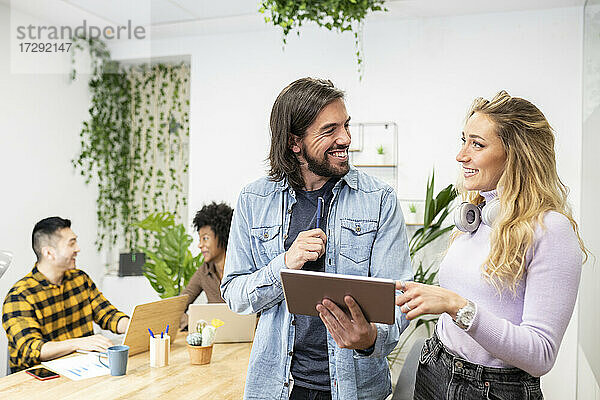 Fröhlicher männlicher und weiblicher Kollege  die sich gegenseitig ansehen  während sie über ein digitales Tablet im Büro diskutieren