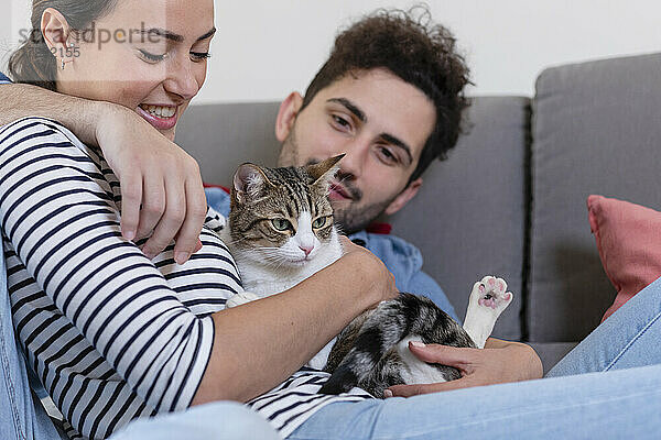 Lächelnder Freund und Freundin spielen mit einer getigerten Katze im Wohnzimmer
