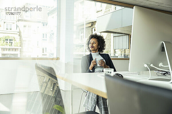 Weibliche Fachkraft mit Kaffeetasse träumt beim Sitzen im Büro