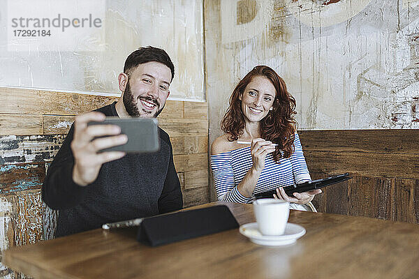 Mann macht Selfie mit einer Kollegin  die ein Grafiktablett in einem Café hält