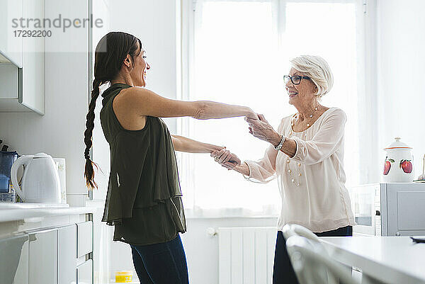 Großmutter und Enkelin halten sich an den Händen und tanzen zusammen in der Küche zu Hause
