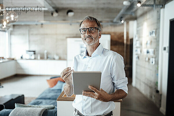 Älterer Geschäftsmann stehend mit digitalem Tablet im Büro